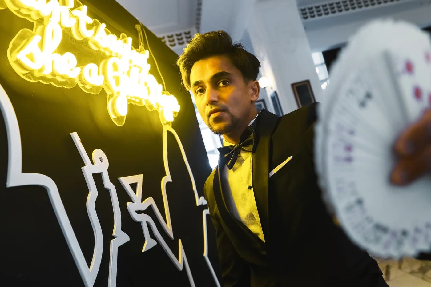 Nabeel in a dinner jacket holds a playing card towards the camera.